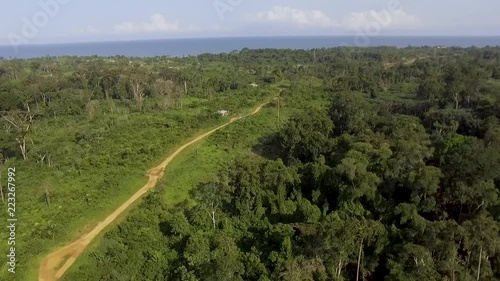 Aerial view of coastline, forest and sea in Kribi in Cameroon, west Africa. Drone moves forward, along dirt road, toward the sea. photo