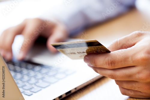 Closeup of a Man Typing on a Laptop and Holding a Credit Card