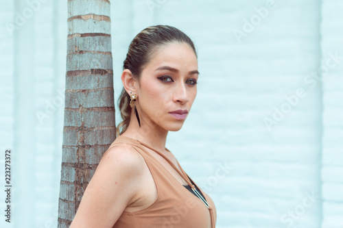 a beautiful slim woman resting on a palm tree looking at the camera in profile, has green eyes and good makeup, photographed in the foreground, model located on the side of the composition