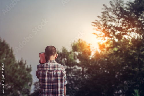 Obraz na plátně Boy raised the Bible on shoulder with ligtf of sunset in mountain background