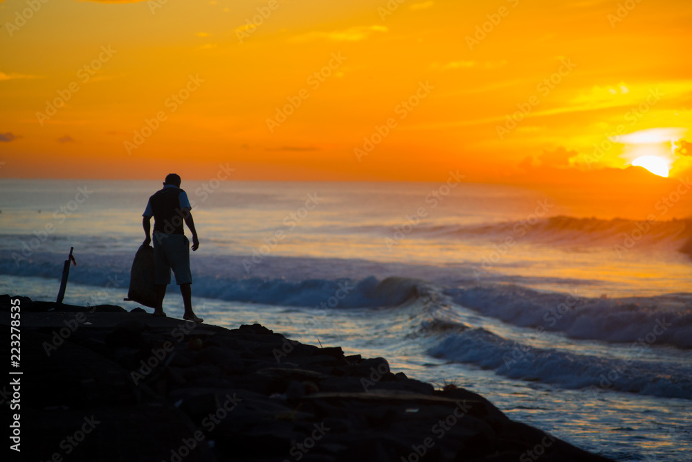 Fototapeta premium An Indonesian Man collecting garbages nearby the ocean of the Bali island, Indonesia. Bali is known as the beautiful ocean view with with exotic culture of Indonesia.