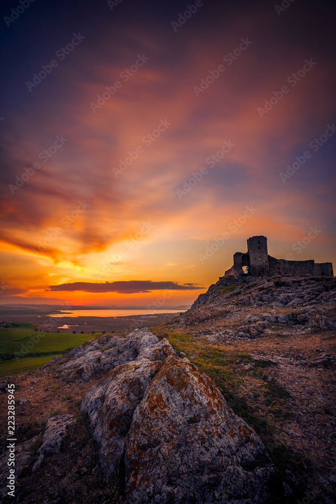 Old ruined citadel on a rocky hill shot at sunset with some rocks in the foreground with dramatic long exposure clouds