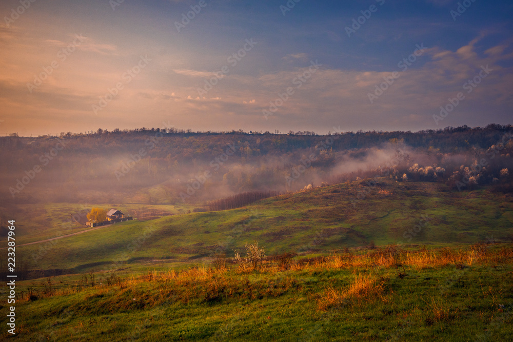 Beautiful morning landscape scene in the village with an isolated house in the background and some fog
