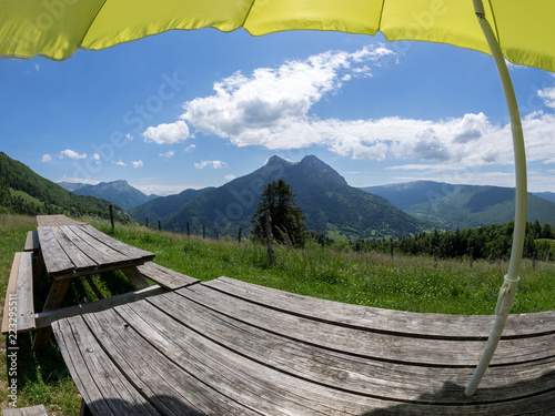 Holztische unter gelbem Sonnenschirm vor hügeliger Kulisse, Refuge des Garins, Haute Savoie, Frankreich