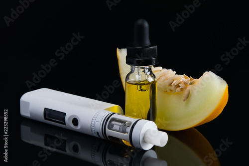 a slice of melon, on a black background, next to the aroma liquid for an electronic cigarette photo