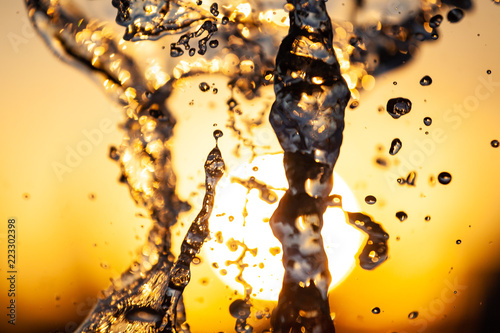 Close-up of a stream of water with droplets and bubbles under the sun on a yellow-orange background. Texture of water waves of a large fountain