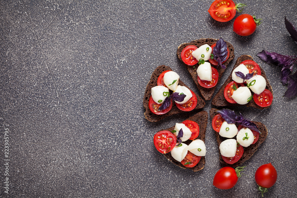 Bruschetta with mozzarella and tomato with basil on black bread