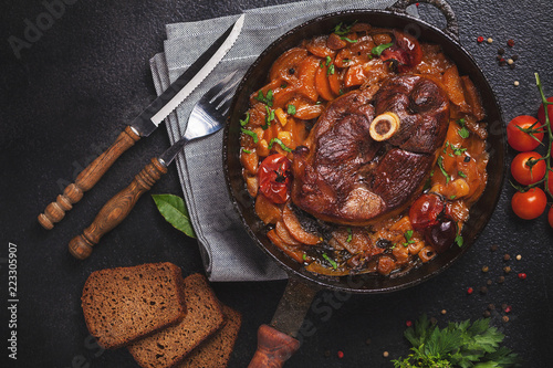 Ready-cooked meat on the bone Osso Buco in tomato sauce over black background of cast iron photo