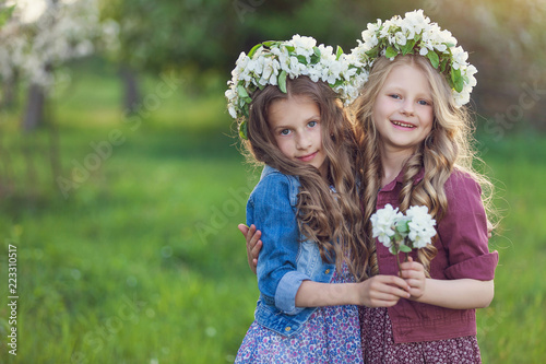 Two cute little girls friends with wreath of flowers in a blooming apple orchard © A.Kazak