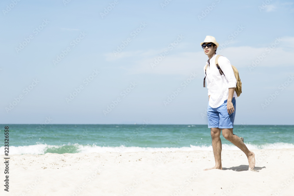 A portrait of hansom asian man in white shirt and blue shorts walking on the beach.Happy classic man on sand at Andaman Sea with beautiful blue sky and clear water. Concept summer vacation holiday.