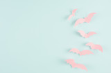 Halloween background for design of cut paper - trendy pink flock bats fly on pastel blue background, copy space.