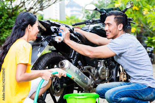 Close-up of happy young couple washing motorcycle at outdoors