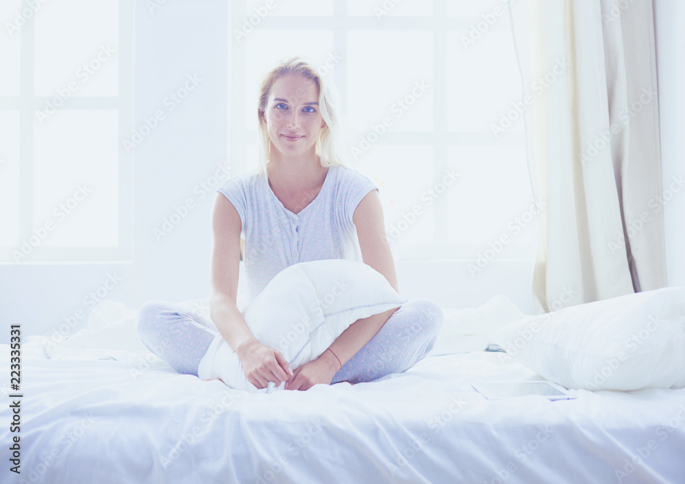 Cute woman holding a pillow while sitting on her bed Cute woman holding a pillow while sitting on her bed