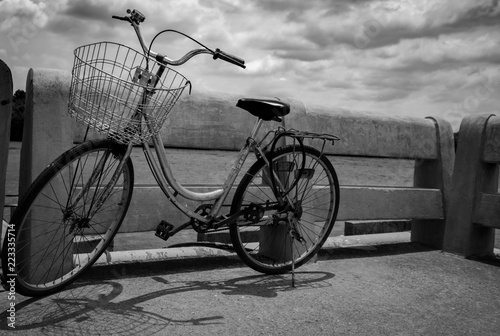 Vintage lonely bicycle parked on concrete road by the river with grey sky and clouds. Travel alone. Lonely life. Worthless or abandoned bike. Hopeless, despair, depressed, sad and grief concept.