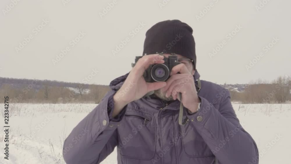 A man takes a picture. shoots on an old camera. Winter season. Warm clothing. Snow field. Bright day. Largest species. 4K video A man takes a picture. shoots on an old camera. Winter season. Warm clothing. Snow field. Bright day. Largest species. 4K video