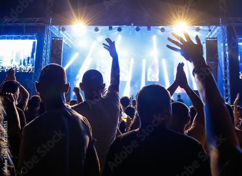 Crowd with raised hands in front of stage with colorful lights.