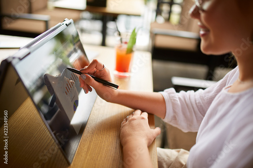 Businesswoman hand pointing with stylus on the chart over convertible laptop screen in tent mode. Woman using 2 in 1 notebook with touchscreen for work on business presentation. Isolated close view.