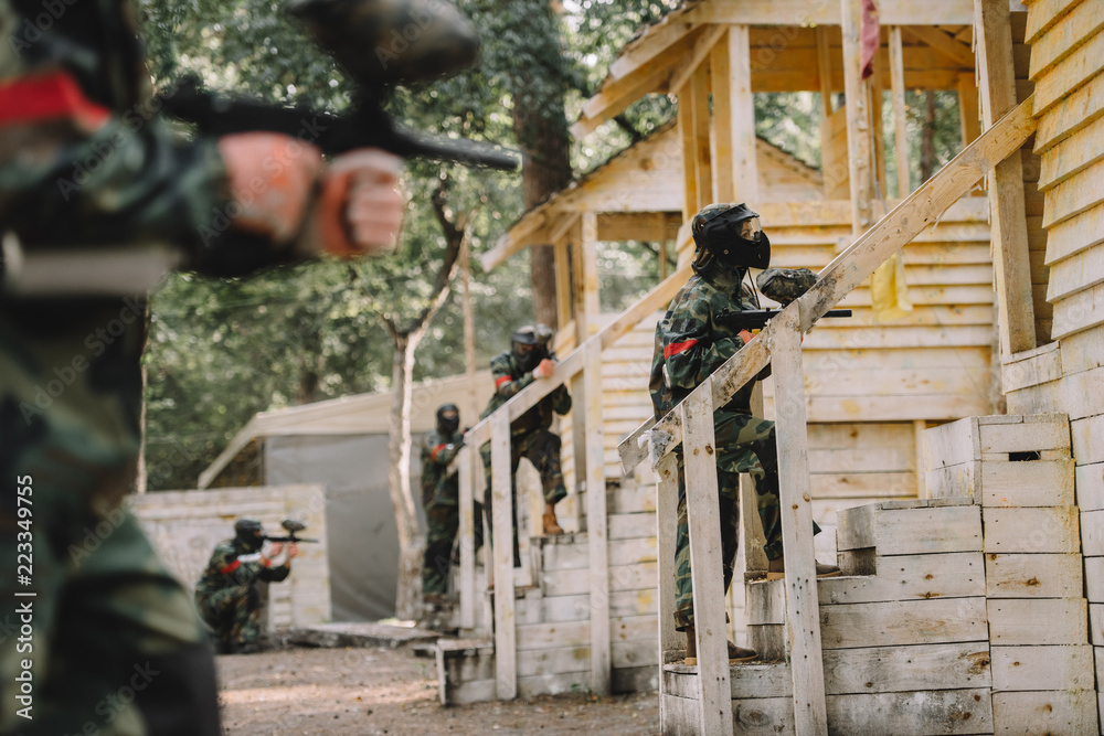 paintball team in uniform and protective masks standing on staircase of wooden towers with paintball guns outdoors