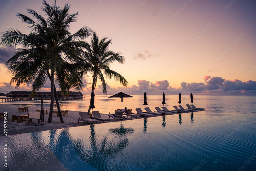 Beautiful poolside and sunset sky. Luxurious tropical beach landscape, deck chairs and loungers and water reflection. Luxurious vacation and holiday, summer beach
