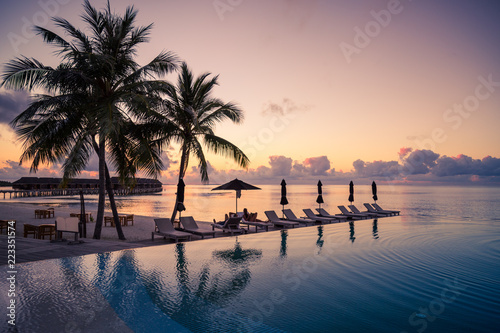 Fototapeta Naklejka Na Ścianę i Meble -  Beautiful poolside and sunset sky. Luxurious tropical beach landscape, deck chairs and loungers and water reflection. Luxurious vacation and holiday, summer beach