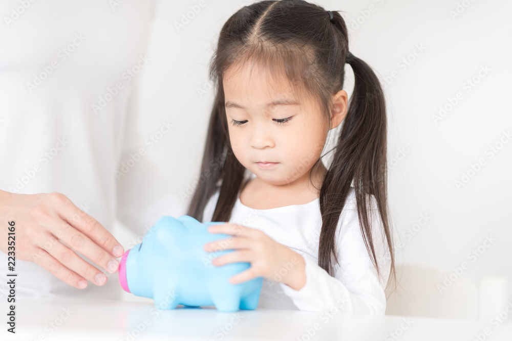 Little girl playing put a coin into piggy bank with father. Educational toy management future lifestyle.Education concept. Little girl playing put a coin into piggy bank with father. Educational toy management future lifestyle.Education concept.