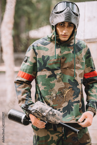 young male paintball player in camouflage covered by paintball splash outdoors