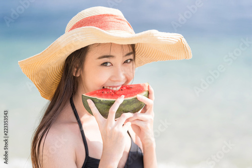 Asain cute girl enjoy eating watermelon on the beach. Happy summer vacation lifestyle concept.