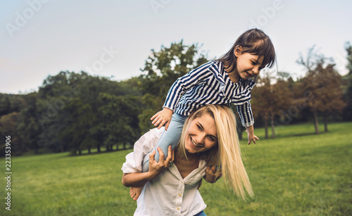 Cute little funny daughter on a piggy back ride with her smiling mother. Loving woman and her little girl playing in the park. Mom and kid have fun outside. Good relationship. Motherhood and parenting