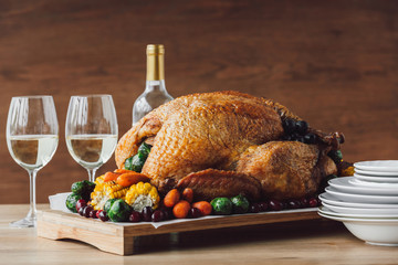 close up view of traditional roasted turkey, vegetables and glasses of wine for thanksgiving dinner