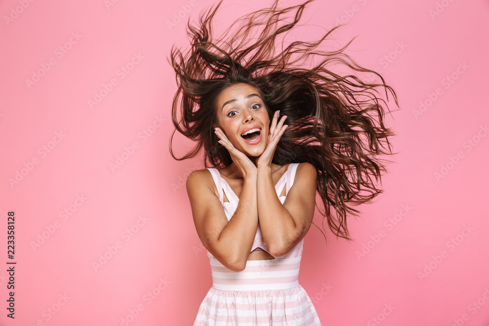 Naklejka premium Photo of beautiful woman 20s wearing dress smiling and shaking her long brown hair, isolated over pink background