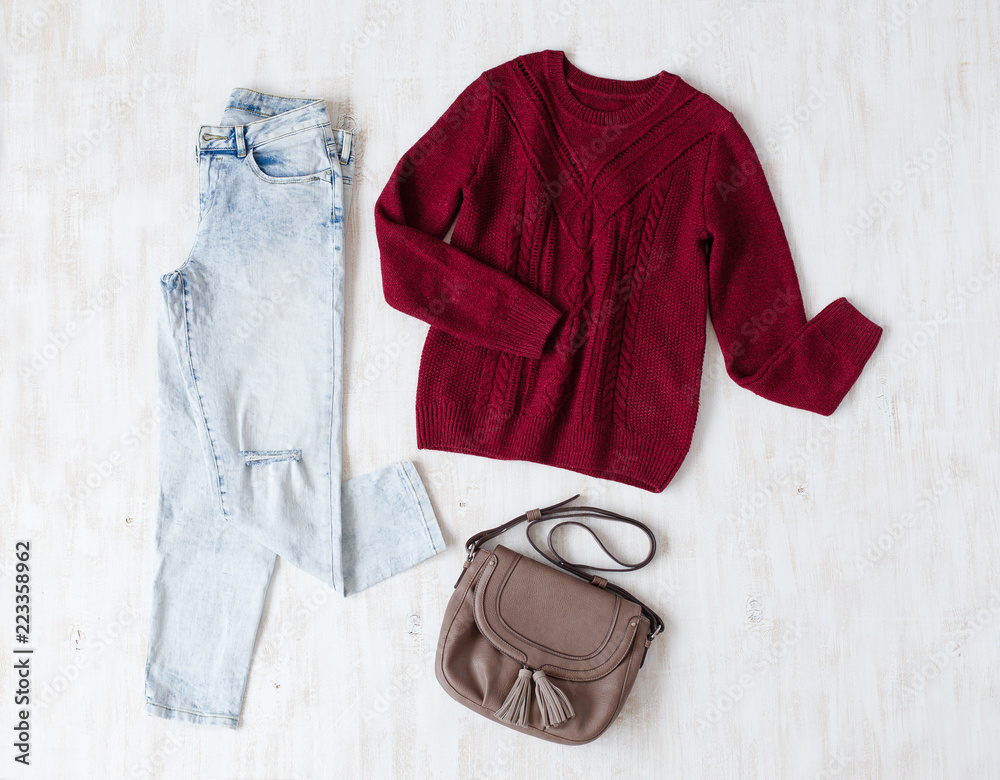 Light blue ripped boyfriend jeans, red oversize knitted sweater and small  brown leather bag with tassels on white wooden background. Overhead view of  woman's casual day outfits. Trendy hipster look. foto de