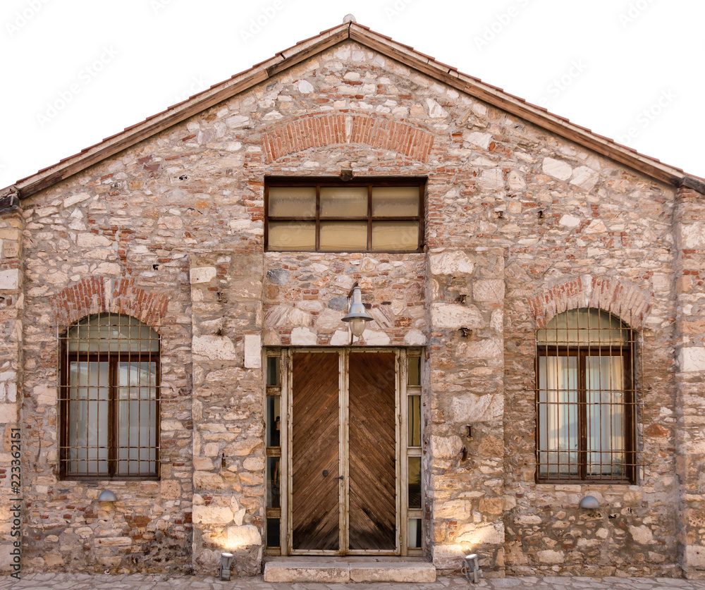 Old stone building with wooden door and two windows with bars.