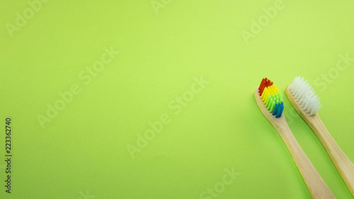 White and rainbow bamboo toothbrushes on green background
