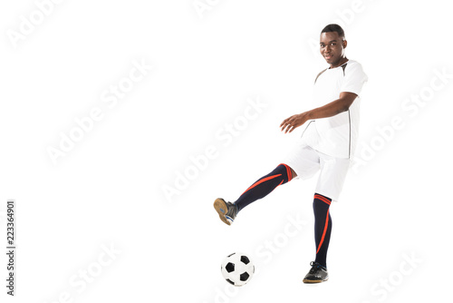 young african american soccer player kicking ball and smiling at camera isolated on white © LIGHTFIELD STUDIOS