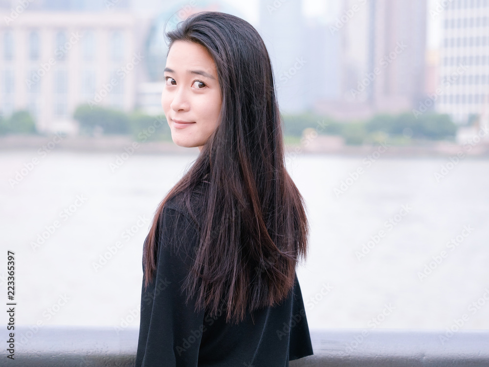 Outdoor portrait of young Chinese girl in black smiling at camera with shanghai bund skyline background, travel and lifestyle concept. Outdoor portrait of young Chinese girl in black smiling at camera with shanghai bund skyline background, travel and lifestyle concept.