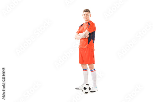 Fototapeta Naklejka Na Ścianę i Meble -  full length view of sporty young soccer player standing with crossed arms and smiling at camera isolated on white