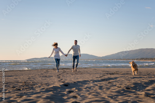 couple with dog having fun on beach on autmun day