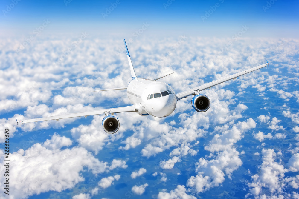 Fototapeta premium Commercial airplane flying over bright blue sky and white clouds.