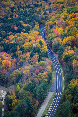 A car driving on a road surrounded by fall color in New England - aerial