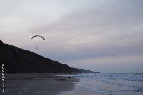 Seascape with silhouettes of the mountains and coast of sea at sunset. Paraglider flying over the beach
