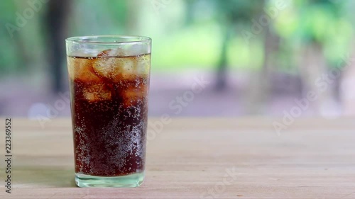 Refreshing black soda soft drinks or cola with ice in a clear tall glass with nature background.