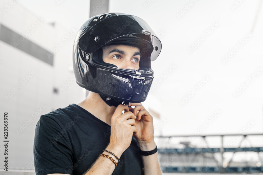 Close up of biker putting on black glossy helmet at urban background. Close up of biker putting on black glossy helmet at urban background.