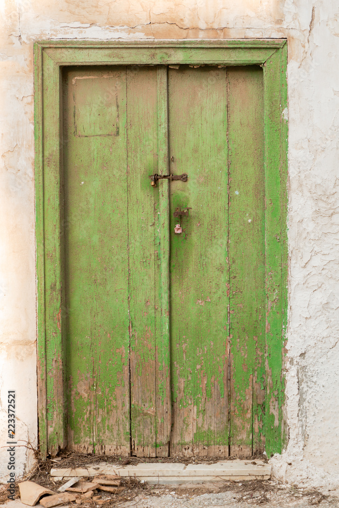 Old green wooden door with cracks, on weathered wall.