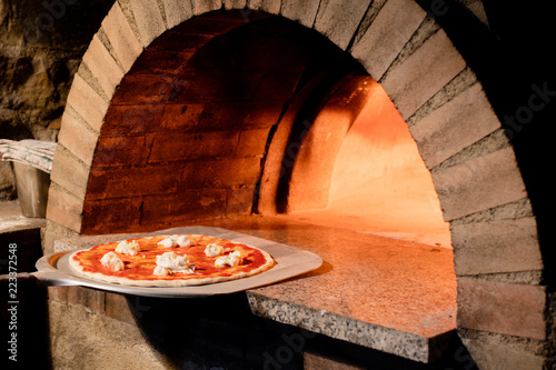 Freshly made pizza being put into hot pizza oven
