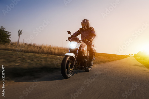 motorcyclist enjoys a ride on her motorbike at sun dawn. the tarmac of the country road shows dynamic unsharpness photo
