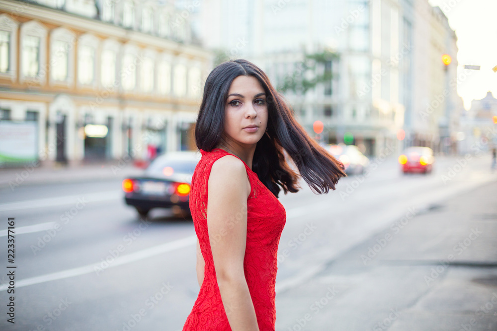 Beautiful Girl in a red dress is standing near of the roadway.