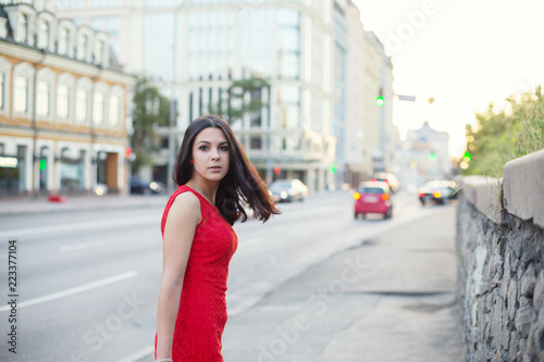 Beautiful Girl in a red dress is standing near of the roadway.