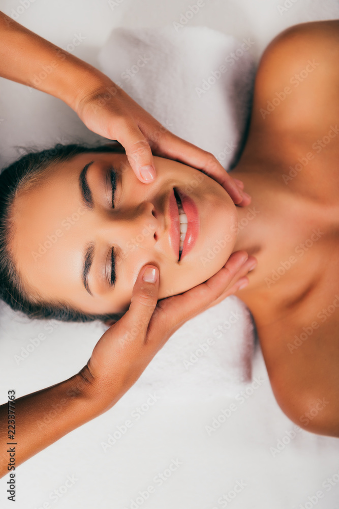 smiling woman relaxing and having face massage in spa salon