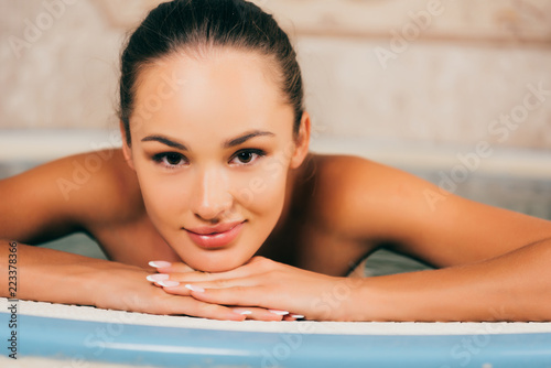 attractive woman resting in swimming pool in spa salon and looking at camera