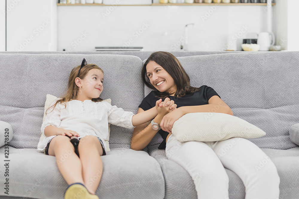 Mother and daughter are having a lot of fun in the living room sitting on the grey couch. mother and daughter holding hands